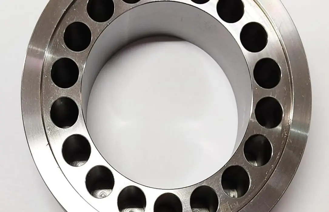 A metal piston component with multiple circular openings around its circumference, displayed on a white background.